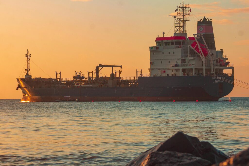 Large oil tanker on the ocean near the coast, sailing under a vibrant sunset sky.