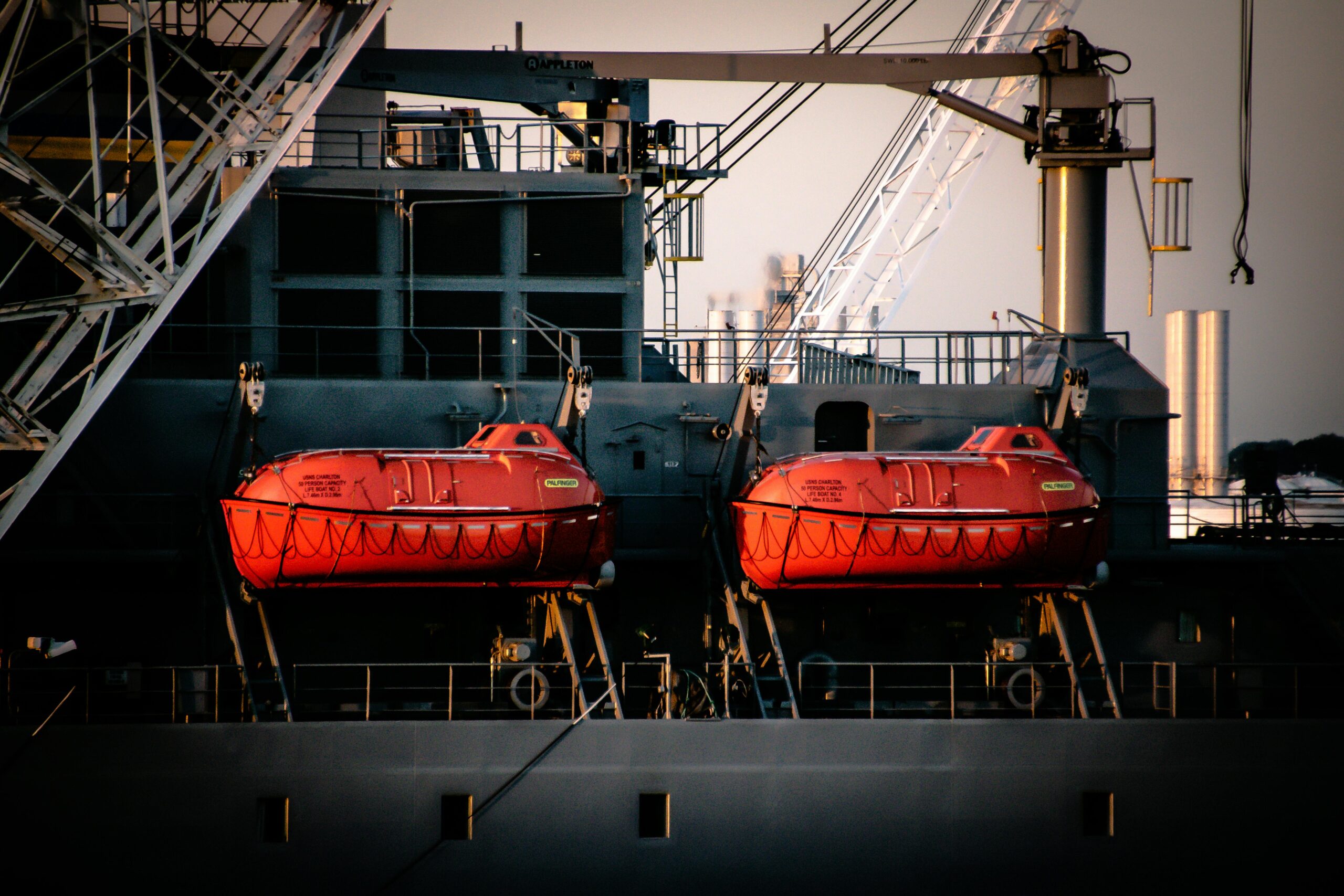 Close-up of a ship displaying two vibrant orange lifeboats attached to its side.