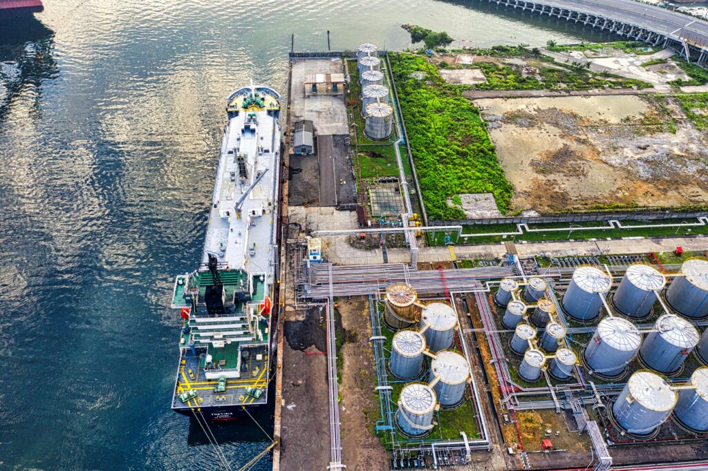 Aerial view of a ship docking at an industrial port with storage tanks in North Jakarta.